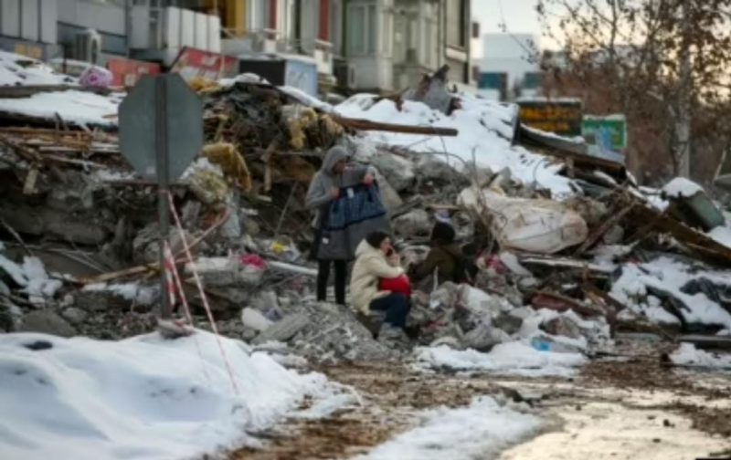 Para penyintas duduk di dekat bangunan yang runtuh di Malatya, Turki, Selasa, 7 Februari 2023. Bantuan mengalir ke Turki dan Suriah saat tim SAR. Sumber foto : voaindonesia.com 