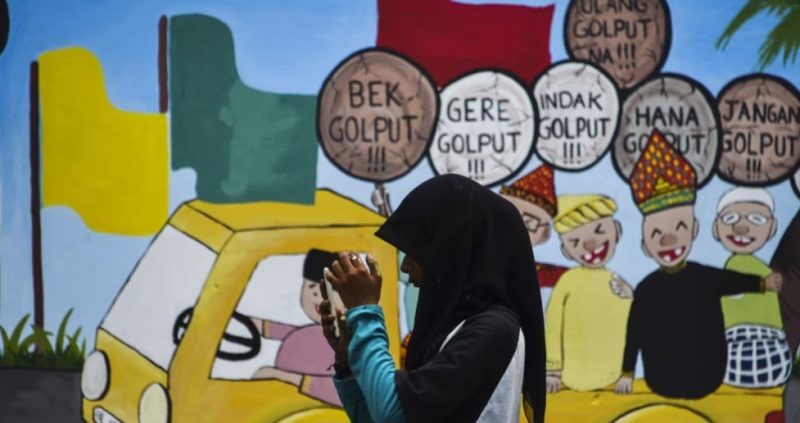Seorang remaja perempuan tampak menggunakan ponselnya di area depan mural kampanye Pemilu 2019 yang terpasang di sebuah lokasi di Banda Aceh, pada 17 Maret 2019. (Foto: AFP/Chaider Mahyuddin)