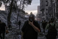 Orang-orang berjalan di atas puing-puing bangunan yang hancur akibat serangan udara Israel di Kota Gaza, Palestina, Sabtu (7/10/2023). [Mohammed ABED / AFP]