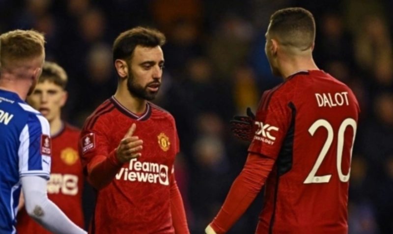 Gelandang Manchester United asal Portugal #08 Bruno Fernandes (tengah) melakukan selebrasi bersama bek asal Portugal #20 Diogo Dalot (kanan) setelah mencetak gol kedua timnya dari titik penalti pada pertandingan putaran ketiga Piala FA 2023-2024 antara Wigan Athletic vs Manchester United di Stadion DW di Wigan, barat laut Inggris pada 8 Januari 2024. Paul ELLIS / AFP.