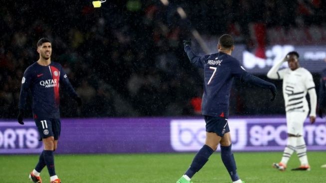 Striker Paris Saint-Germain Kylian Mbappe (kanan) melemparkan pita kapten tim kepada bek Paris Saint-Germain Achraf Hakimi saat meninggalkan lapangan setelah ditarik keluar dari lapangan dalam laga Rennes melawan PSD di Stadion Parc des Princes, Paris, Prancis, pada 25 Februari 2024. (sumber: suara.com)