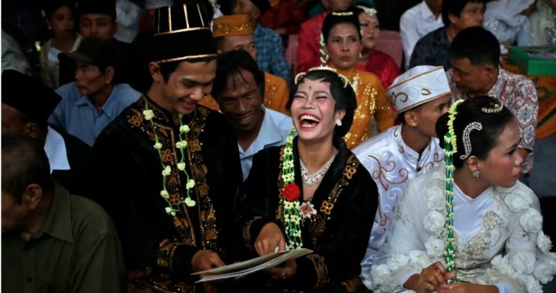 Sepasang pengantin tertawa gembira membaca surat nikah mereka saat pernikahan massal yang digelar di Jakarta (foto: ilustrasi). 