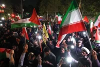 Demonstran mengibarkan bendera Iran dan bendera Palestina saat mereka berkumpul setelah Iran melancarkan serangan drone dan rudal ke Israel di depan Kedutaan Besar Inggris di Teheran, Iran, Minggu (14/4/2024) (sumber: suara.com)