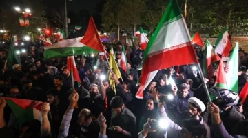 Demonstran mengibarkan bendera Iran dan bendera Palestina saat mereka berkumpul setelah Iran melancarkan serangan drone dan rudal ke Israel di depan Kedutaan Besar Inggris di Teheran, Iran, Minggu (14/4/2024) (sumber: suara.com)