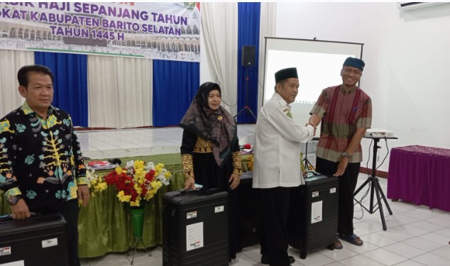 Nurdin, Kasi Penyelenggara Haji dan Umrah Kantor Kemenag Kabupaten Barsel (baju putih) saat menyerahkan koper haji kepada CJH yang siap berangkat menunaikan ibadah haji tahun 2024 secara simbolis, di Aula Kantor Kemenag setempat, Selasa (23/4/2024). Foto. Alifansyah/1tulah.com