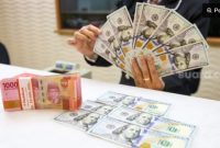 Petugas salah satu tempat penukaran mata uang asing menunjukkan uang rupiah dan dolar AS, Jakarta, Selasa (14/1/2025). [Suara.com/Alfian Winanto]