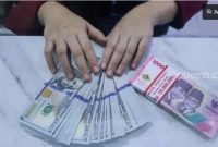 Ilustrasi petugas menunjukkan mata uang Rupiah dan Dolar AS. [Suara.com/Alfian Winanto] 