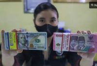 Ilustrasi petugas menunjukkan mata uang Rupiah dan Dolar AS di tempat penukaran uang. [Suara.com/Alfian Winanto] 