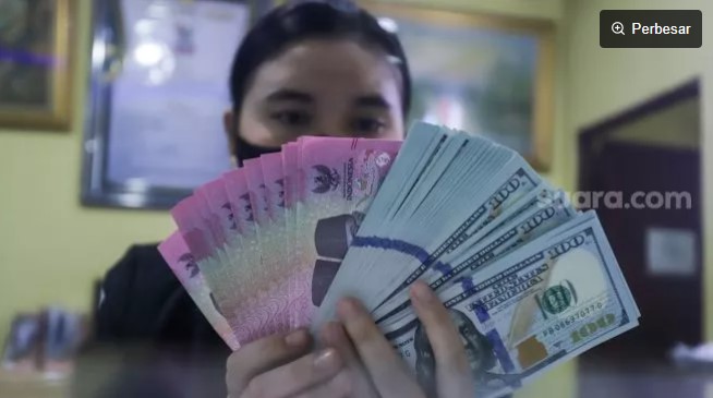 Ilustrasi petugas menunjukkan mata uang Rupiah dan Dolar AS di tempat penukaran uang. [Suara.com/Alfian Winanto]