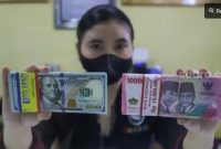 Petugas menunjukkan mata uang Rupiah dan Dolar AS di tempat penukaran uang, Jakarta. [Suara.com/Alfian Winanto] 