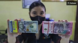Petugas menunjukkan mata uang Rupiah dan Dolar AS di tempat penukaran uang, Jakarta. [Suara.com/Alfian Winanto] 